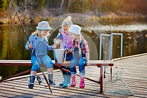 Three little happy girls brag about fish caught on a fishing pole. Fishing from a wooden pontoon