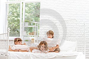 Three little happy kids playing on bed at home