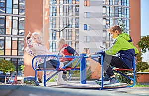 Three little kids playing on merry-go-round outdoors in spring.