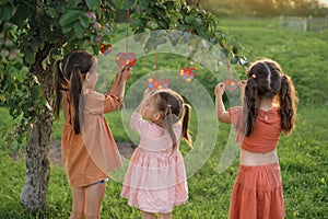 Three little sister girls hang heart-shaped postcards with colored puzzles