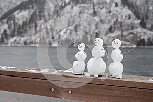 Three little snowmen standing on the railing. River embankment in winter, the river is not frozen. Copy space.
