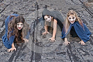 Three little teenage girls in zombie costumes crawl along the roof of an old ruined building and look frighteningly at the camera photo