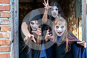 Three little teenage girls in zombie costumes go out the door of an old ruined building and look frighteningly at the camera. photo