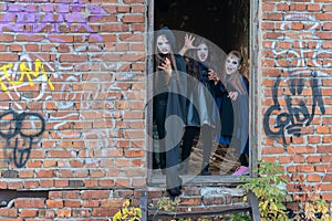 Three little teenage girls in zombie costumes go out the door of an old ruined building and look frighteningly at the camera. photo
