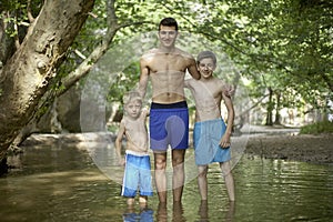 Three loving brothers standing in shallow water in a beautiful forest, family feeling love taking care