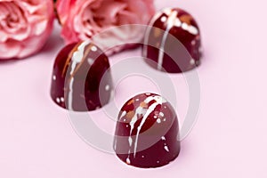 Three Luxury Bonbons Painted with White Colors on Pink background Beautiful and Exclusive Handmade chocolate Candy and Roses