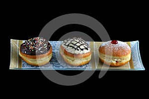 Three luxury sufganiyot with different icing on a decorative plate