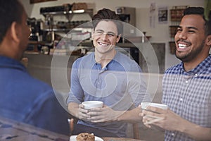 Three male friends laughing over coffee at a coffee shop