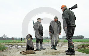 Three male hunters and dog with hares. low perspective. Rural area. Winter season. Proud hunting dog sitting with the catch.