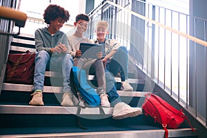 Three Male Secondary Or High School Pupils Inside School Building On Stairs With Digital Tablet photo