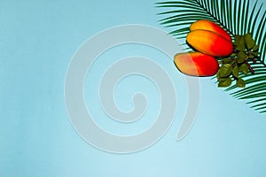 three mangoes on a palm leaf in the upper right corner of a blue background, creative summer concept