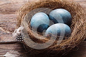 Three marble blue Easter eggs painted by hibiscus, in a nest on a wooden background close-up. The Symbol Of Easter