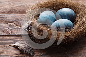 Three marble blue Easter eggs painted by hibiscus, in a nest on a wooden background close-up. The Symbol Of Easter