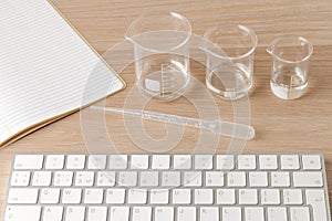 Three measuring beakers with a measuring pipette with notebook and a keyboard