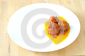 Three meatballs on a white dish, with tomato sauce