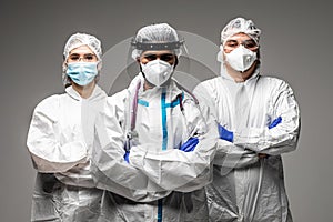 Three medical healthcare workers in biohazard protective tools standing isolated on gray background. Ready to fight with covid19