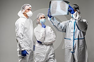 Three medical healthcare workers exam x-ray at meeting in biohazard protective tools standing isolated on gray background. Ready