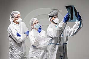 Three medical healthcare workers exam x-ray at meeting in biohazard protective tools standing isolated on gray background. Ready