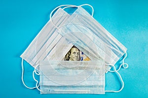 Three medical masks lie on 100 dollars banknote on blue background. Concept of deficit, speculation of face masks