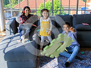 Three members of mixed races family, father, mother and kid daughter live together in home living room. Girl throwing toy with dad