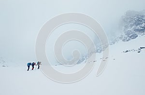 Three members rope team ascending the high mountain winter peak. Blizard covering the structural basin in Vysoke Tatry (High