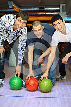 Three men bent over to heave up balls for bowling