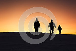 Three men descend from the top in the mountains after climbing at sunset.