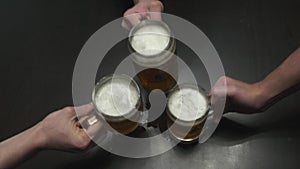 Three men drinking lager near the bar counter. Close up of male hands clinking their glasses top view. Caucasian guys