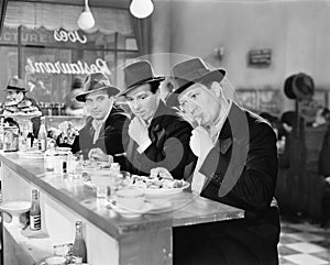 Three men with hats eating at the counter of a diner photo