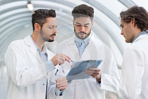 Three men in labcoats looking at clipboard