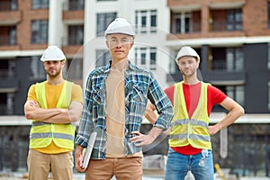 Three men in protective helmets standing on the building site