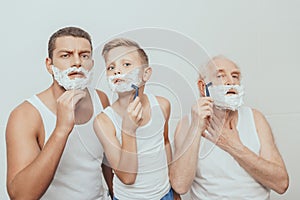 Father son and grandfather standing with shaving cream on their faces shaving with razors photo