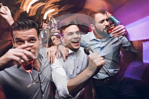 Three men sing at a karaoke club. Young people have fun in a nightclub. They are very cheerful and they smile.