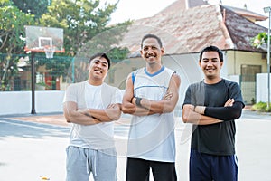 three men standing on the edge of an outdoor basketball court