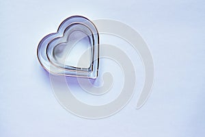 Three metal cookie cutters in heart shape on light blue background with copy space