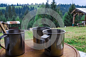 Three metal cups with morning coffee in the campaign against the background of the mountains covered with forests