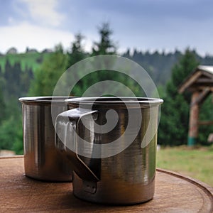 Three metal cups with morning coffee in the campaign against the background of the mountains covered with forests