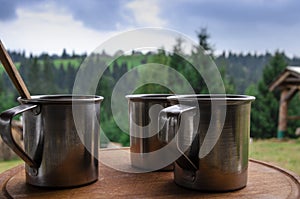 Three metal cups with morning coffee in the campaign against the background of the mountains covered with forests
