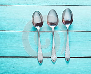 Three metal spoons on a blue wooden background. Top view.