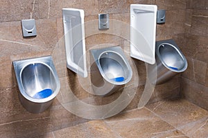 Three metal urinals with automatic water flush sensor after urinate, Men`s toilet trimmed with brown marble tiles photo