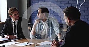 Three millennial businessmen negotiating meet in modern boardroom