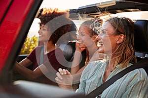 Three millennial female friends on a road trip driving together in an open jeep, close up