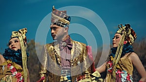 Three models in elaborate traditional costumes with intricate headpieces against a clear blue sky