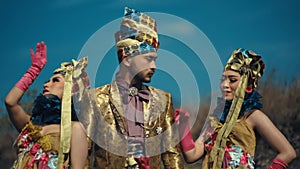 Three models in elaborate traditional costumes with intricate headpieces against a clear blue sky