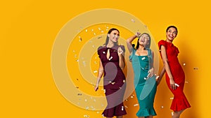Three Models Posing Under Falling Silver Confetti, Yellow Background, Panorama