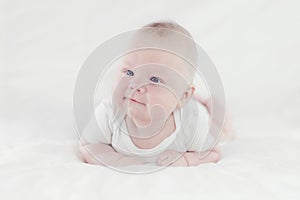 Three-month caucasian boy in white clothes lying on his belly on white blankets