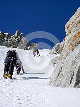 Three mountain climbers on a steep north face heading up a narrow couloir