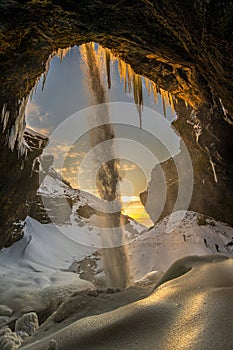 Three mountaineering tourists in front of the frozen Kvernufoss waterfall, with snow and stalagmites and falling water illuminated