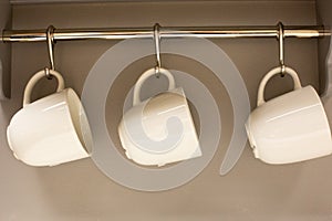 Three mugs weigh on hangers in a home corner in the kitchen.