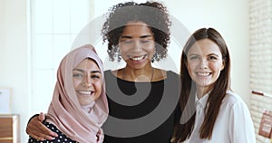 Three multicultural smiling young women friends embracing looking at camera